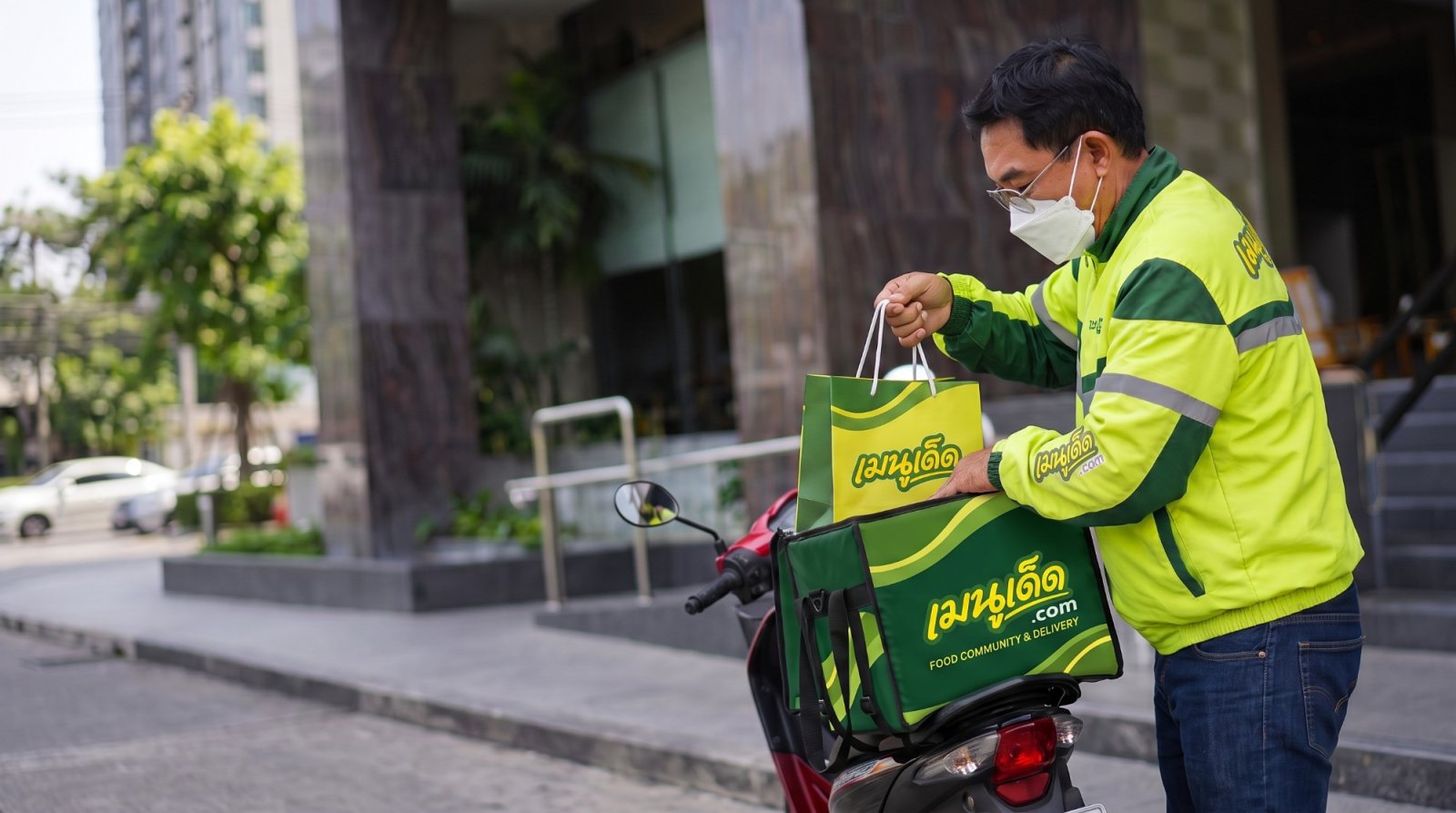 ไรเดอร์เมนูเด็ดในชุดแจ็กเก็ตสีเขียว กำลังใส่ถุงอาหารลงกล่องส่งอาหารเมนูเด็ด